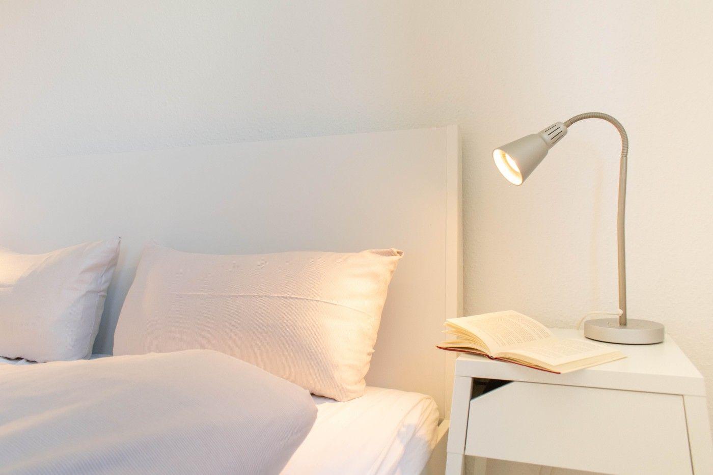 Schlafzimmer mit Bett, Nachttisch und Stehlampe. Ein Buch liegt auf dem Tisch.