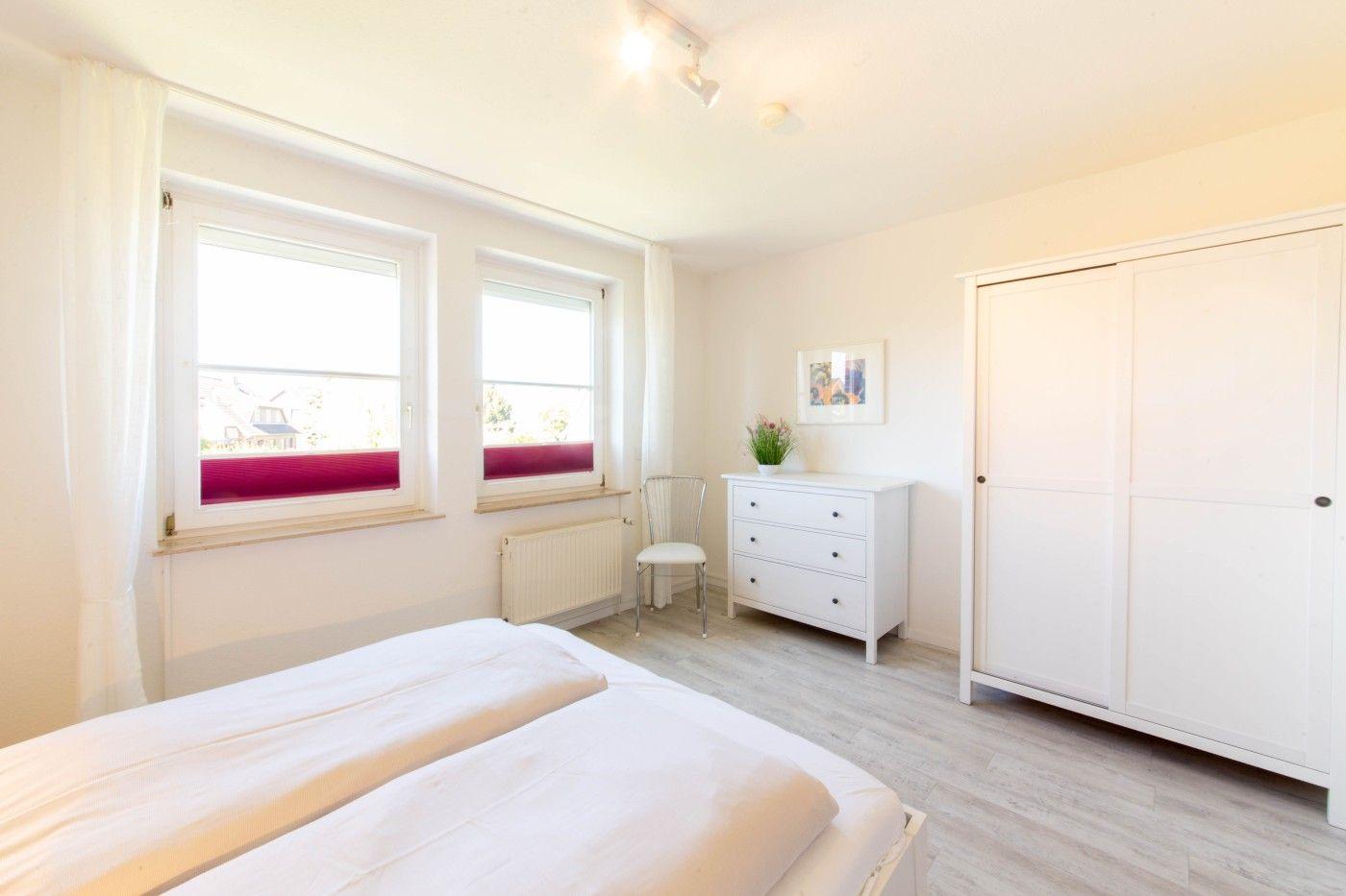 Schlafzimmer mit Doppelbett, zwei Fenstern, Schrank und Schreibtisch.