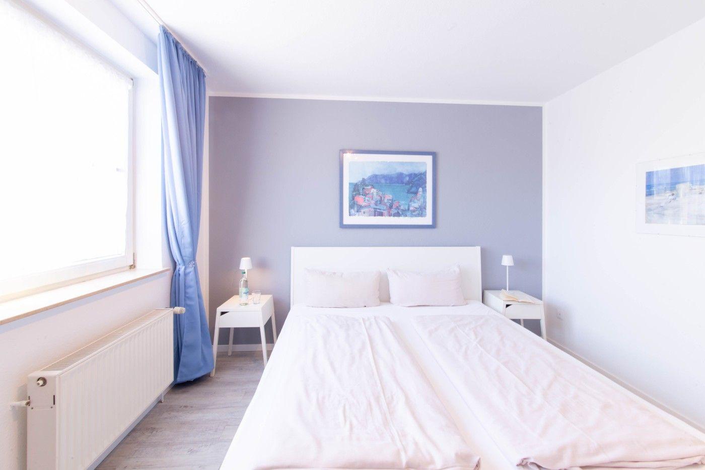Schlafzimmer mit Bett, zwei Nachttischen und Fenster mit Vorhängen.