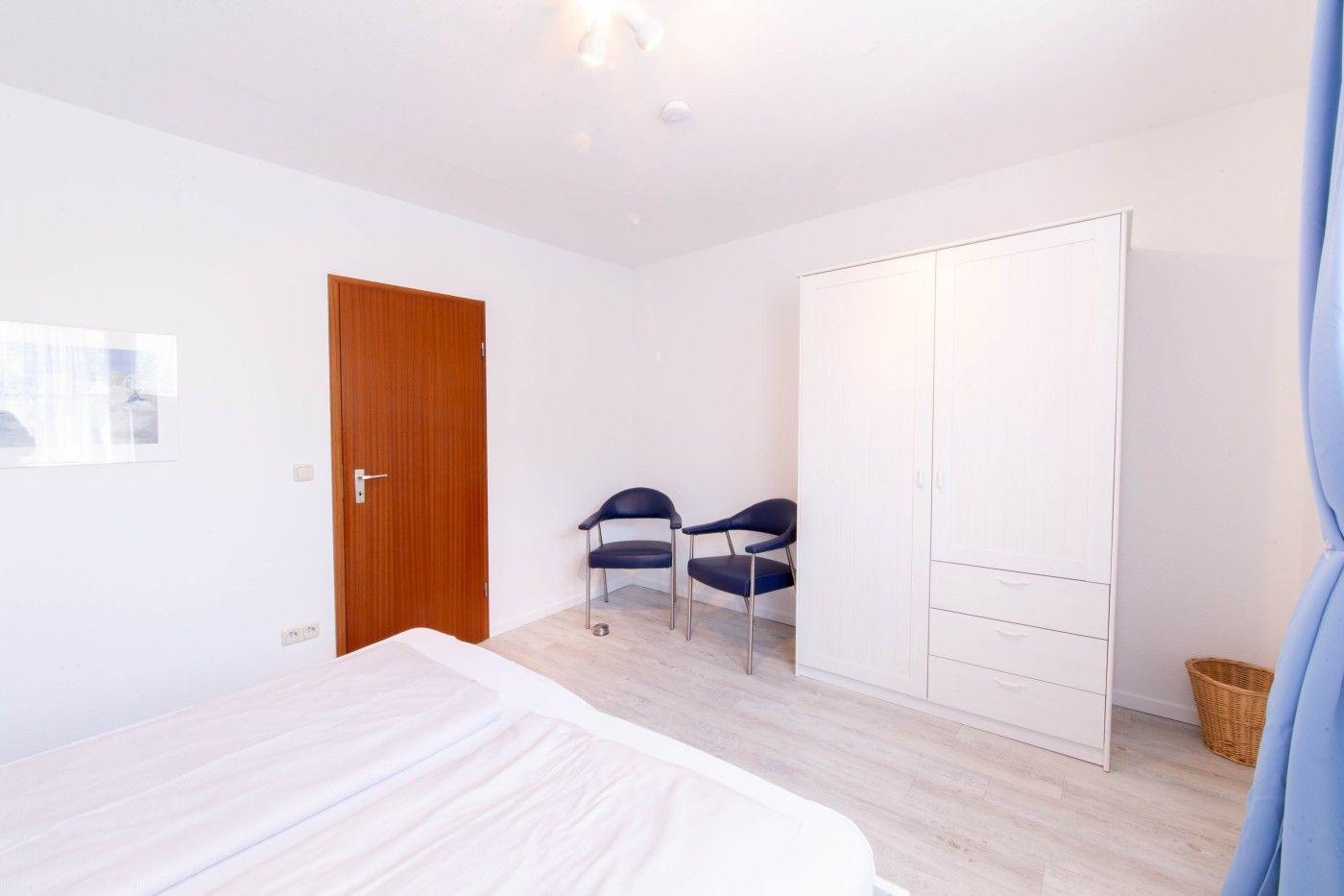 Schlafzimmer mit Bett, Kleiderschrank, zwei Stühlen und Holztür.