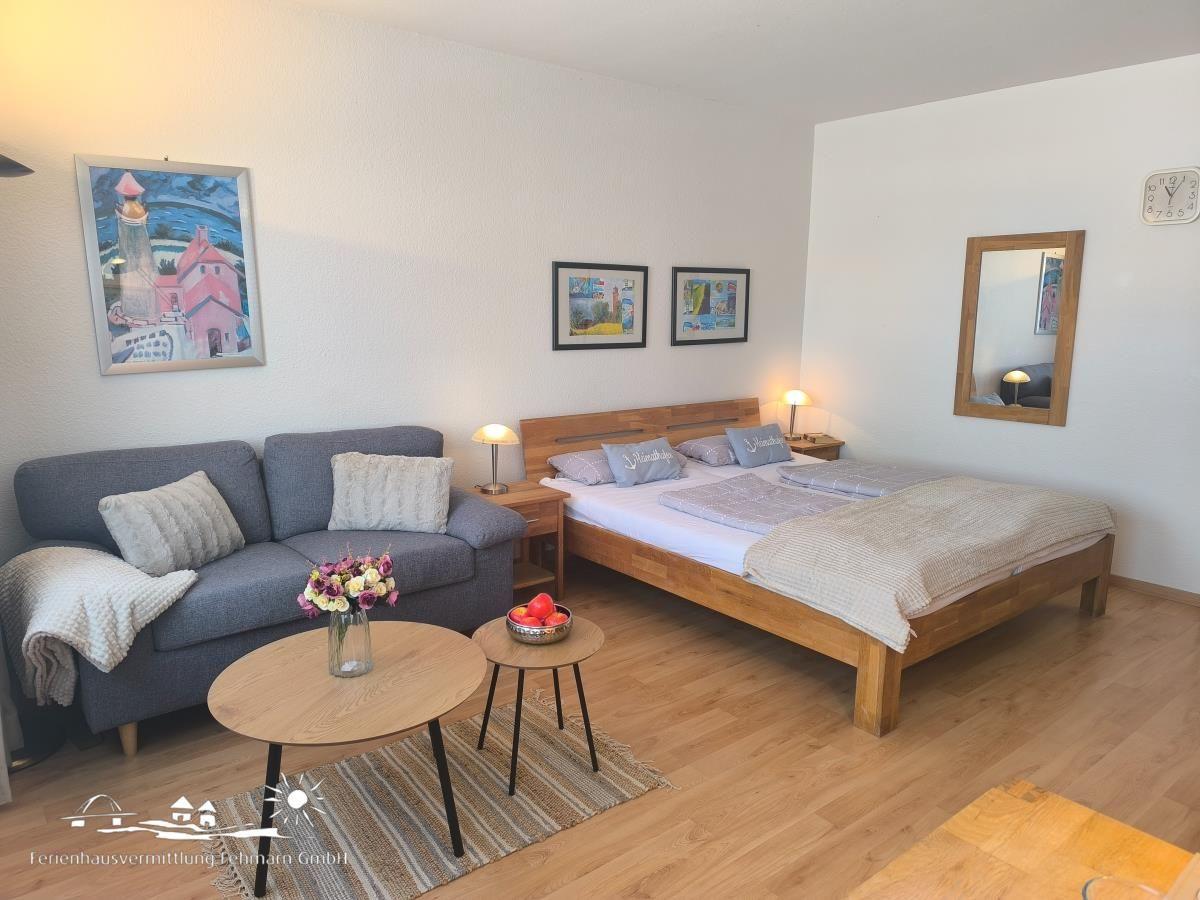 Schlafzimmer mit Bett, Sofa, Tisch und Wandbildern.
