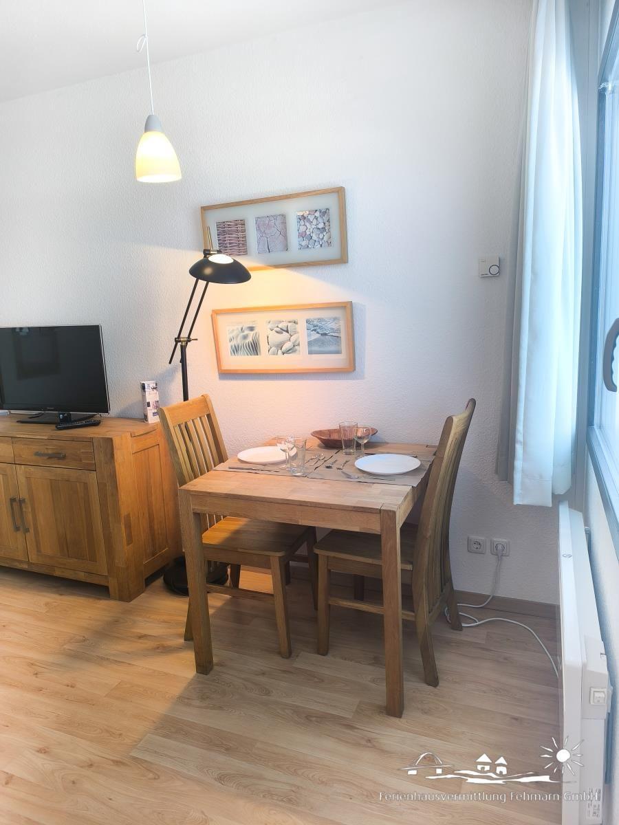 Essbereich mit Holztisch, zwei Stühlen, TV und Fenster.
