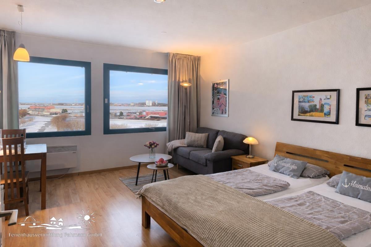 Zimmer mit Doppelbett, Sofa, Tisch und zwei Fenstern mit Blick auf Hafen.