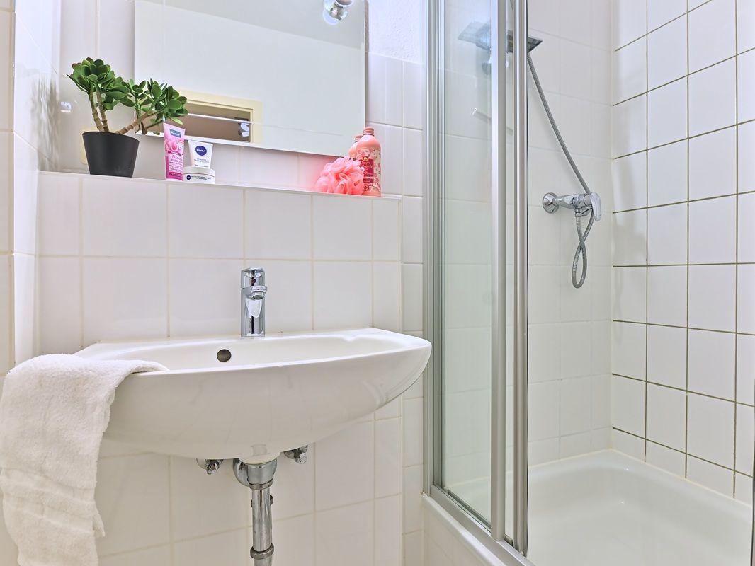 Badezimmer mit Waschbecken, Dusche und Pflanze auf der Ablage.