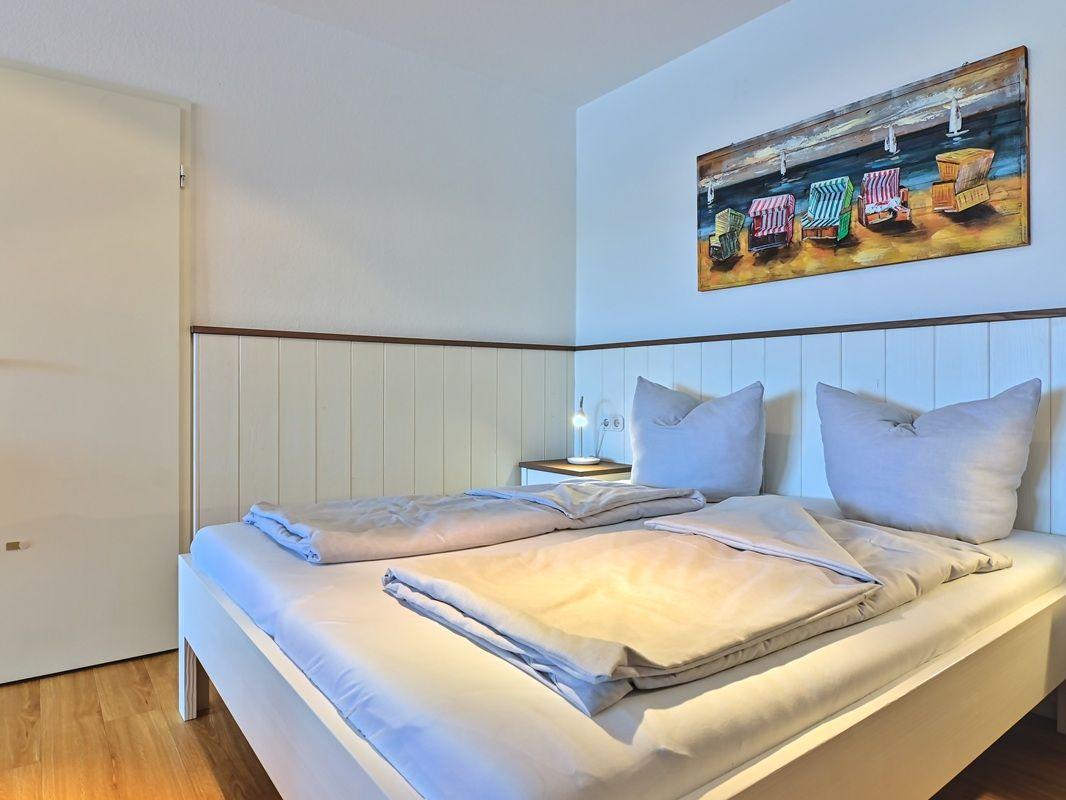 Schlafzimmer mit Bett, Wandbild und Holzverkleidung an der Wand.