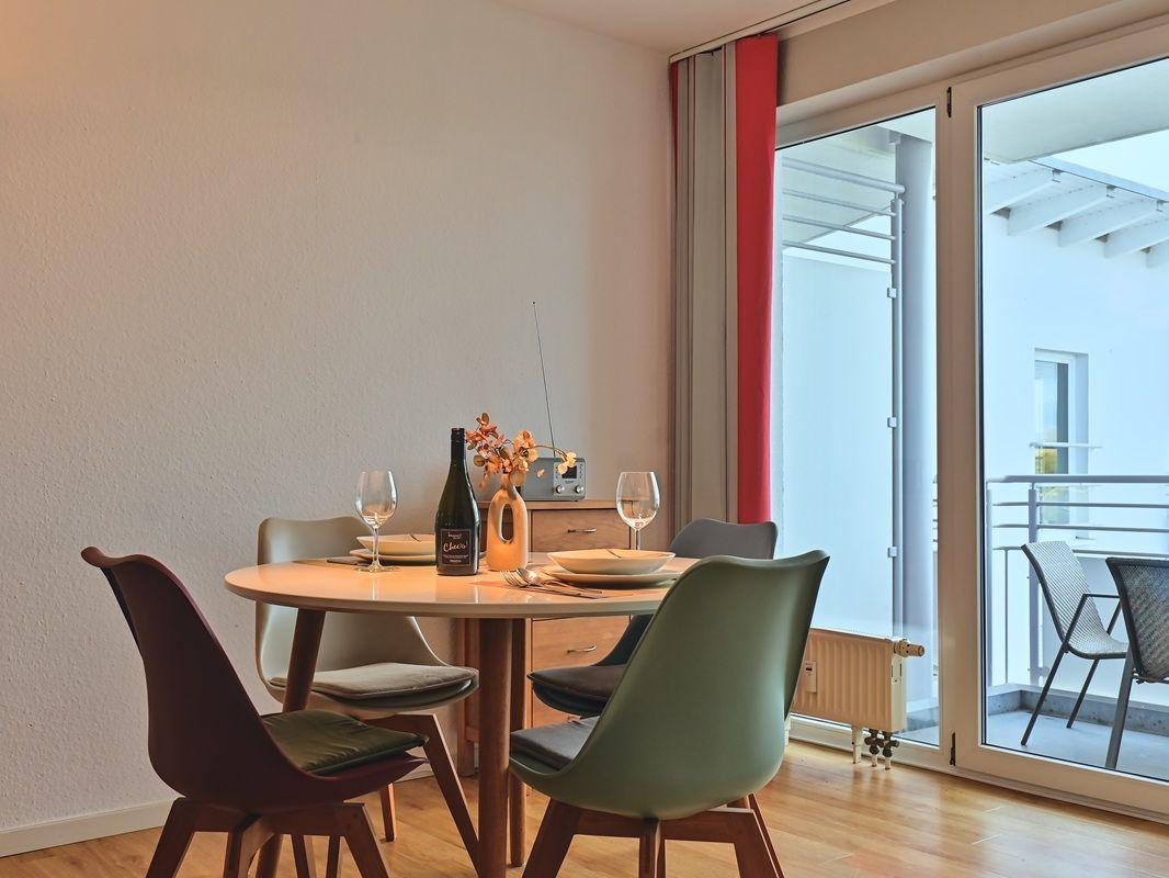 Rundtisch mit Stühlen, Flasche und Gläsern. Durchgang zur Terrasse mit Sitzgelegenheiten.