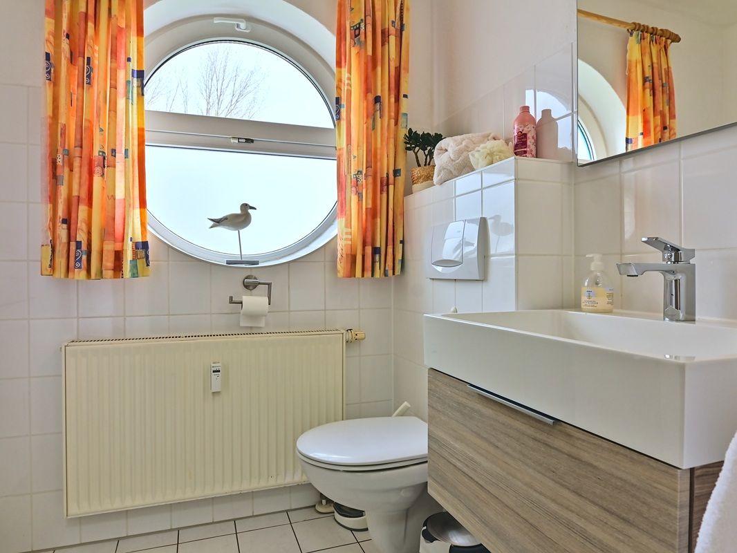 Badezimmer mit runden Fenster, Toilette und Waschbecken.