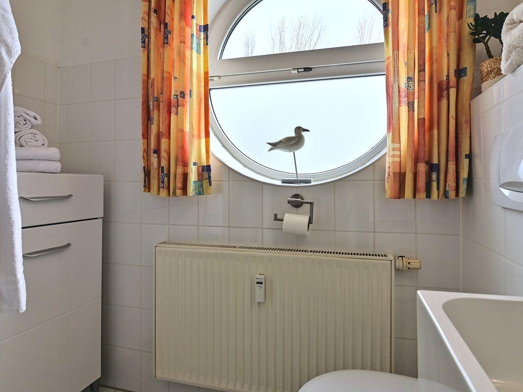 Badezimmer mit runden Fenster, orangefarbenen Vorhängen und Seemöwe-Dekoration.