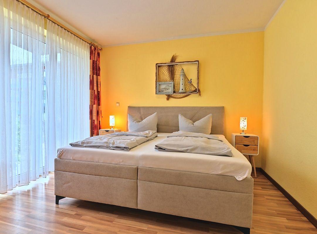 Schlafzimmer mit Doppelbett, gelben Wänden und Holzboden. An der Wand hängt ein dekoratives Bild.