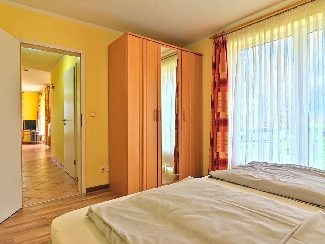 Schlafzimmer mit Bett, Kleiderschrank und Fenster mit Vorhängen.