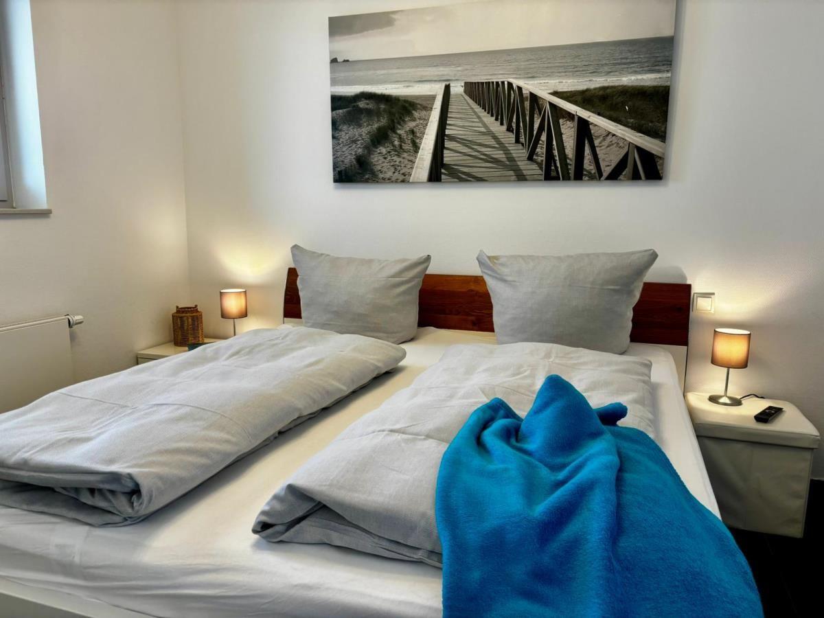 Zimmer mit Doppelbett, zwei Nachttischen und Wandbild mit Strandmotiv.