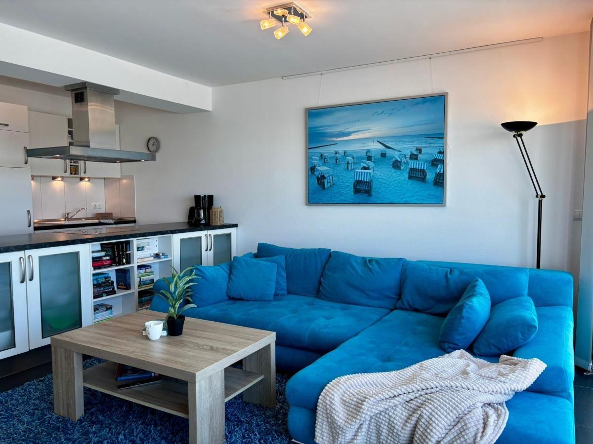 Ein Wohnzimmer mit blauem Sofa, Küchenbereich und Wandbild mit Strandmotiv.
