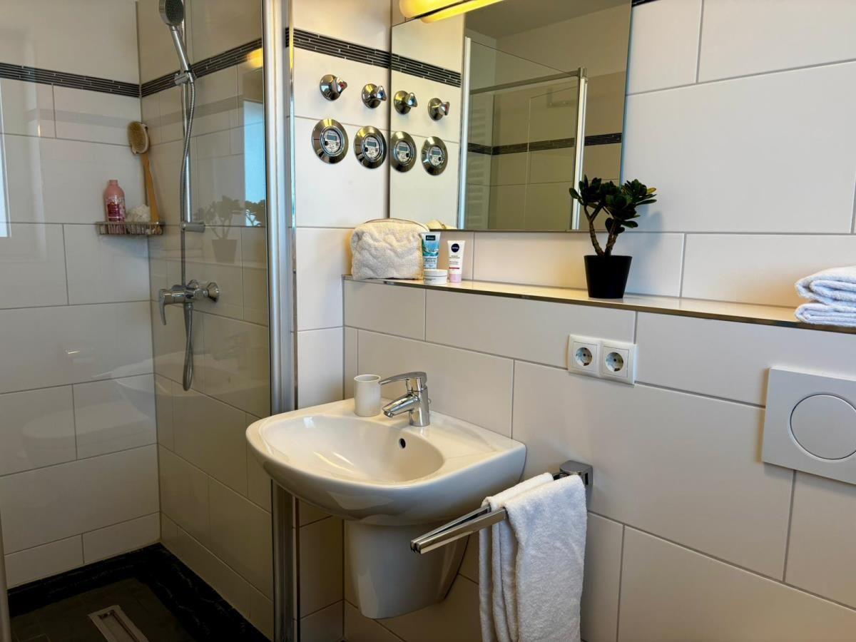 Badezimmer mit Dusche, Waschbecken und Spiegel. Kleine Pflanze und Handtücher sind vorhanden.