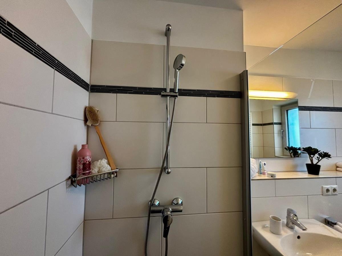 Dusche mit Duschbrause, Spiegelschrank und Waschbecken im Badezimmer.