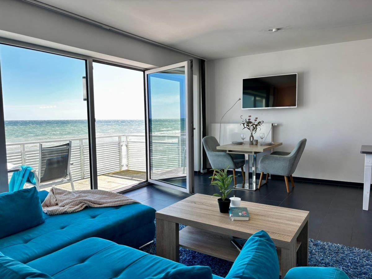 Wohnzimmer mit Blick aufs Meer, blaue Couch, Esstisch und TV.