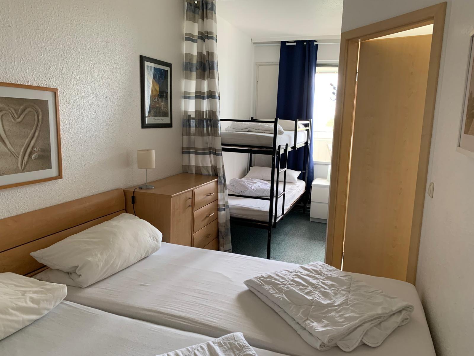 Zimmer mit Doppelbett und Schlafcabinen im Hintergrund. Holzmöbel und Wandbilder.