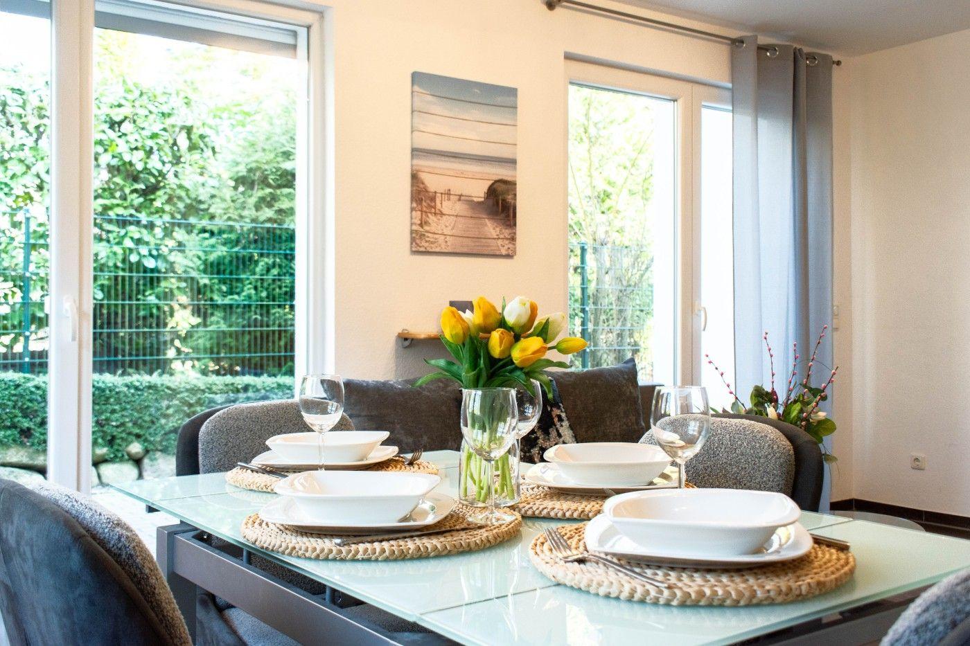 Glasglastisch mit vier Plätzen, Blumen und Blick auf Garten.