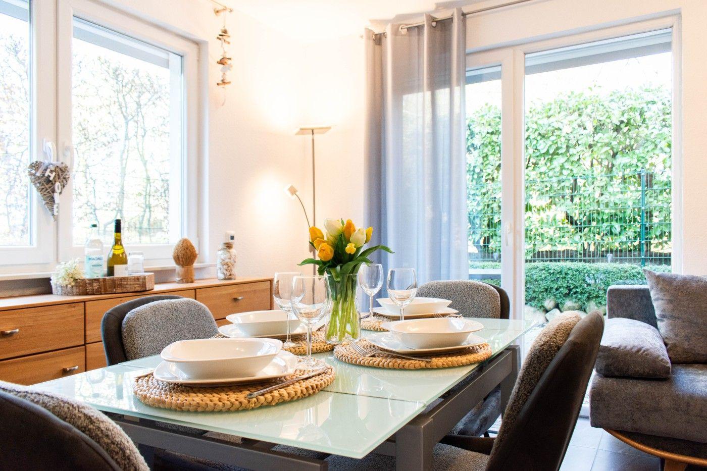 Essbereich mit Glasplatte, Stühlen und Blumen. Fenster zur grünen Außenseite.
