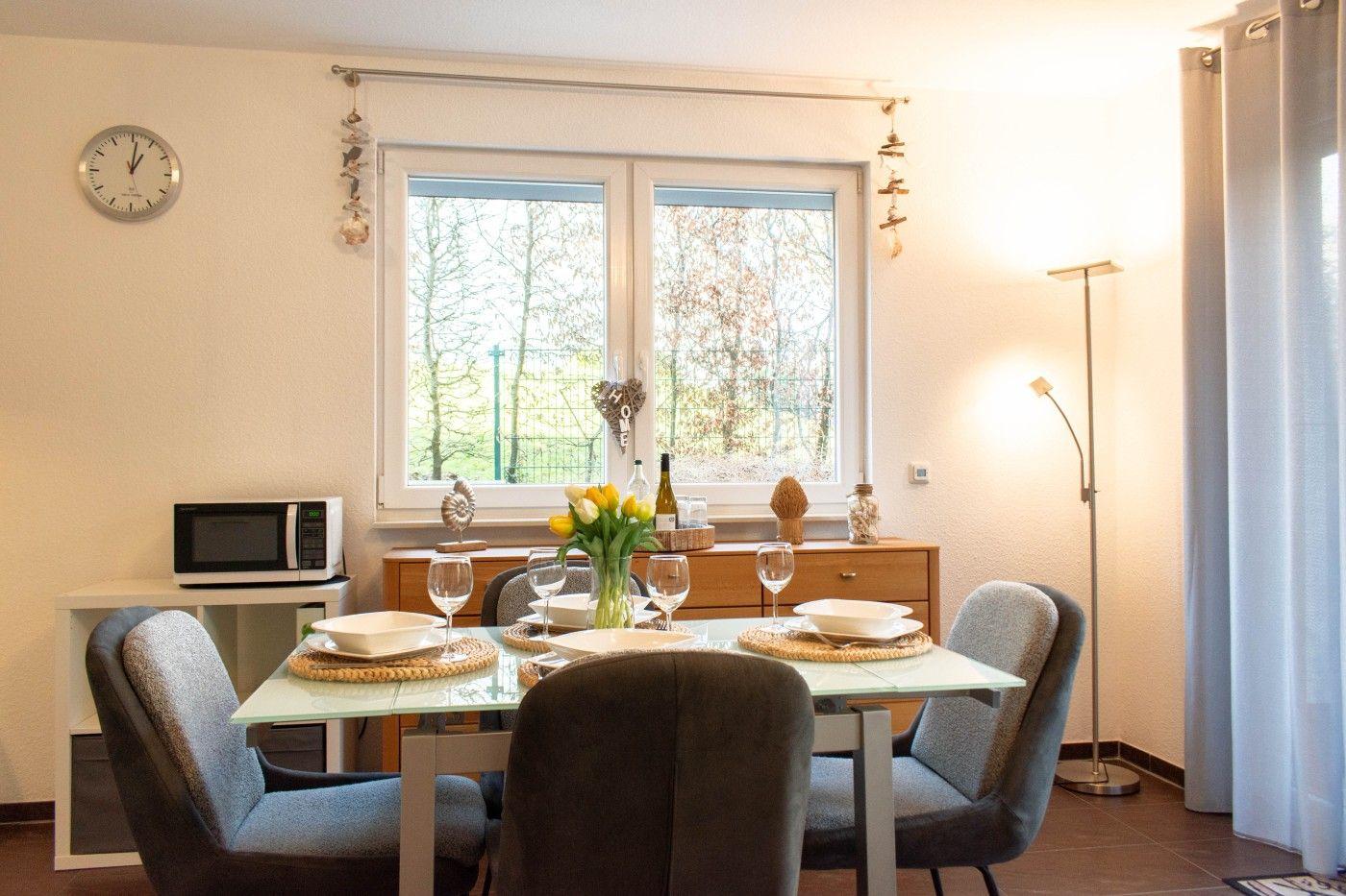 Esszimmer mit Tisch, Stühlen und Fensterblick auf Grünfläche.