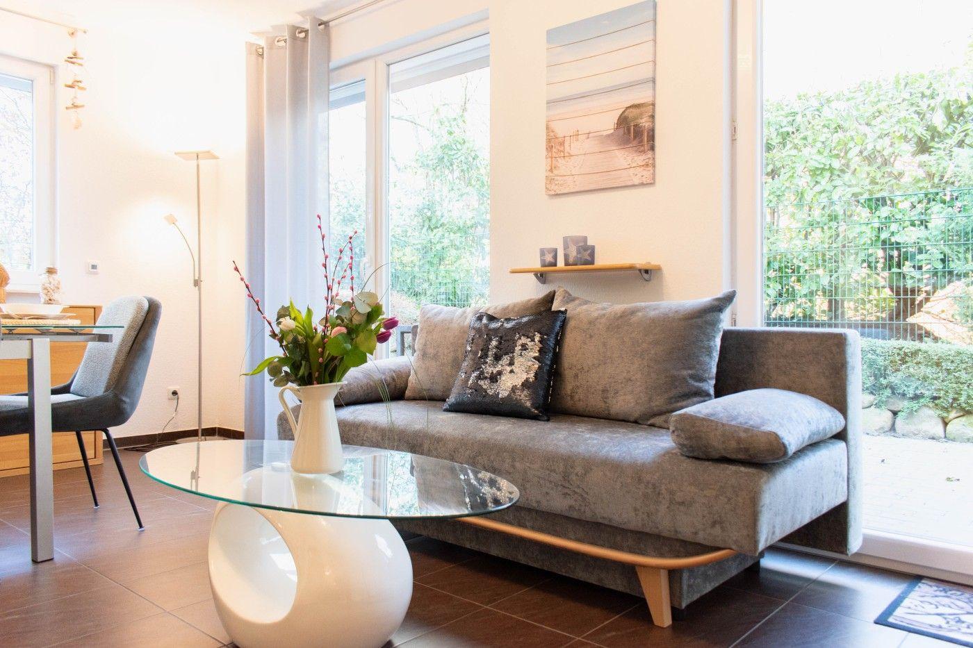 Wohnzimmer mit grauem Sofa, Glas-Tisch und Blick auf Garten.