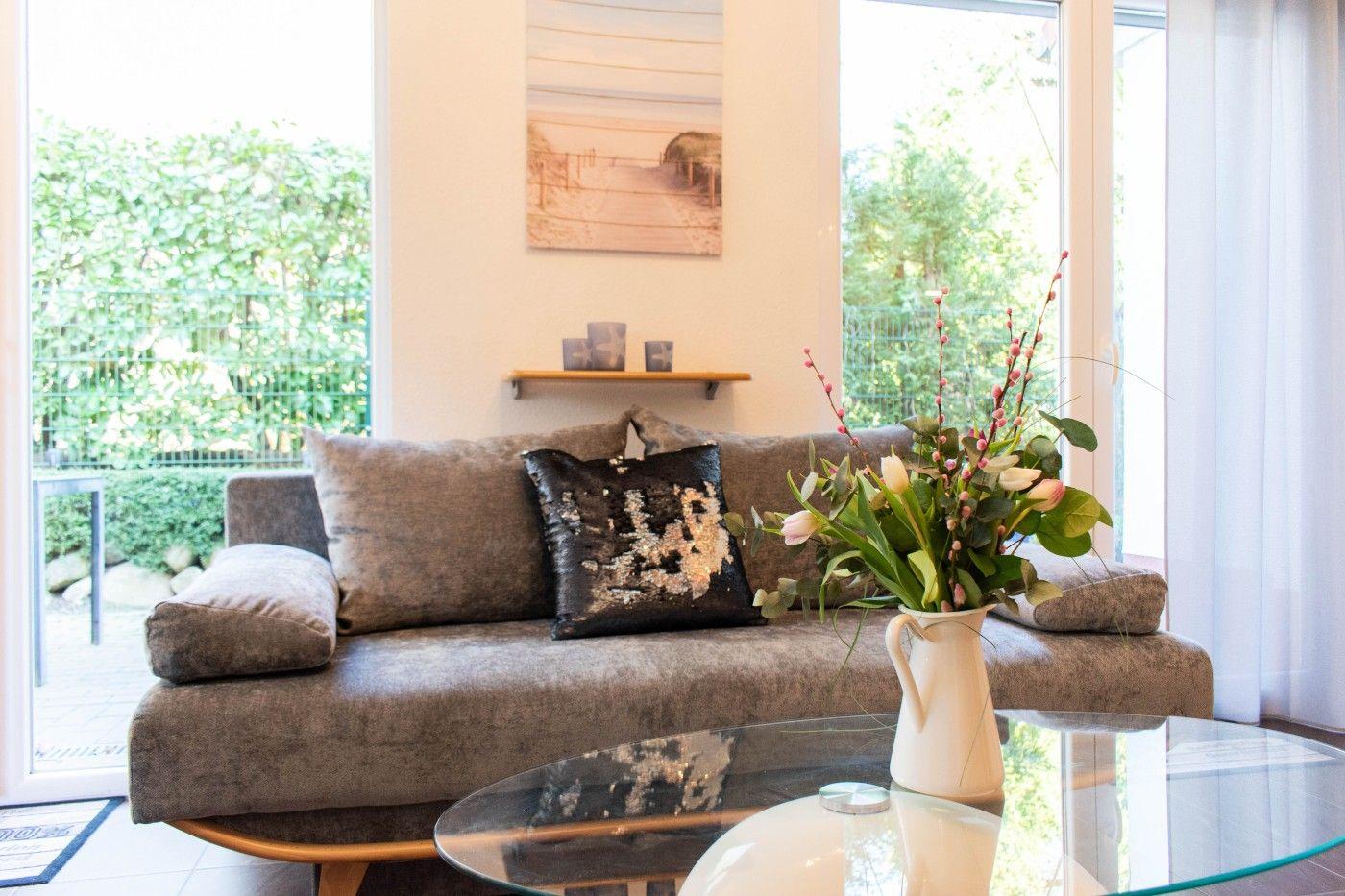 Ein Sofa mit Kissen und Blumen auf einem Tisch vor Fenstern.