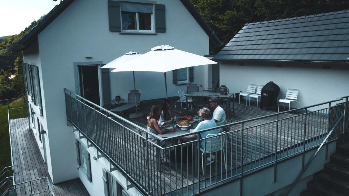 Gruppen sitzen auf einer Terrasse mit Tisch, Stühlen und Sonnenschirmen.