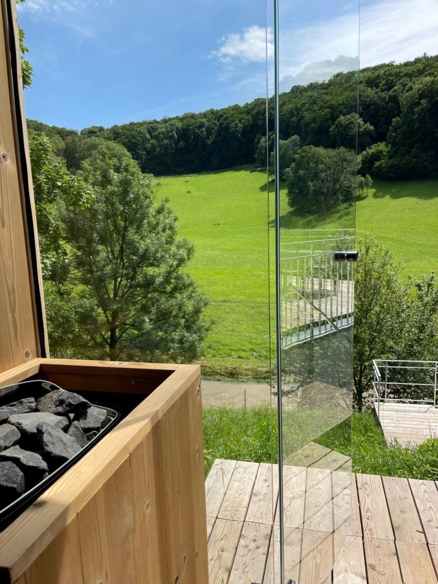 Terrasse mit Glasgeländer und Blick auf grünes Feld und Wald.