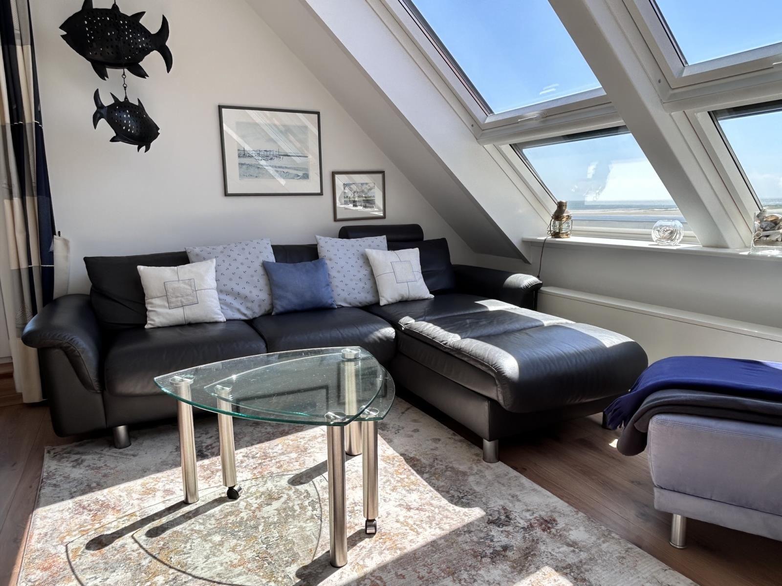 Schwarzes Sofa mit Kissen unter Dachfenster. Glas-Tisch auf Teppich.
