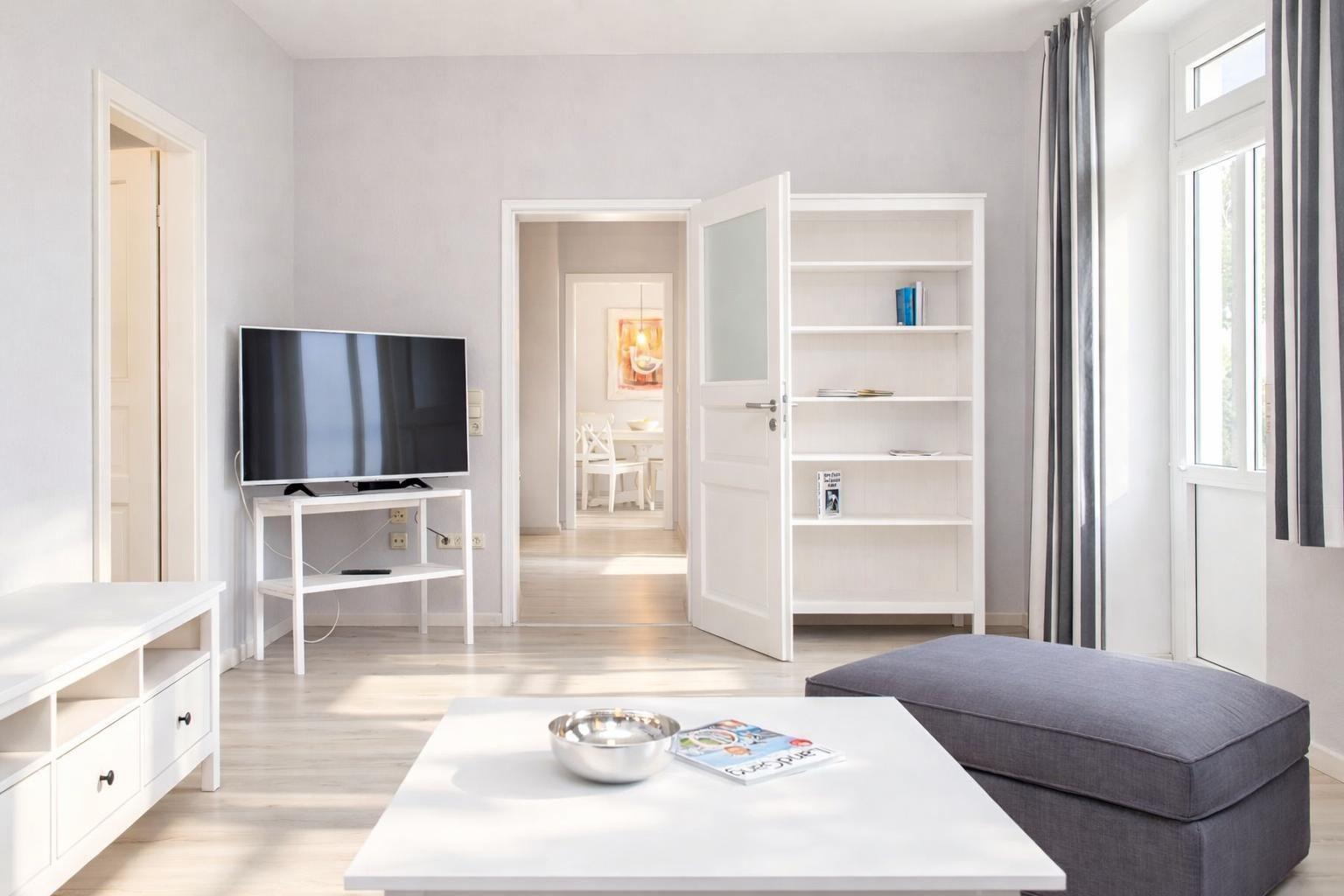 Living room with TV, bookcase, and seating. Passage to dining and bedroom.
