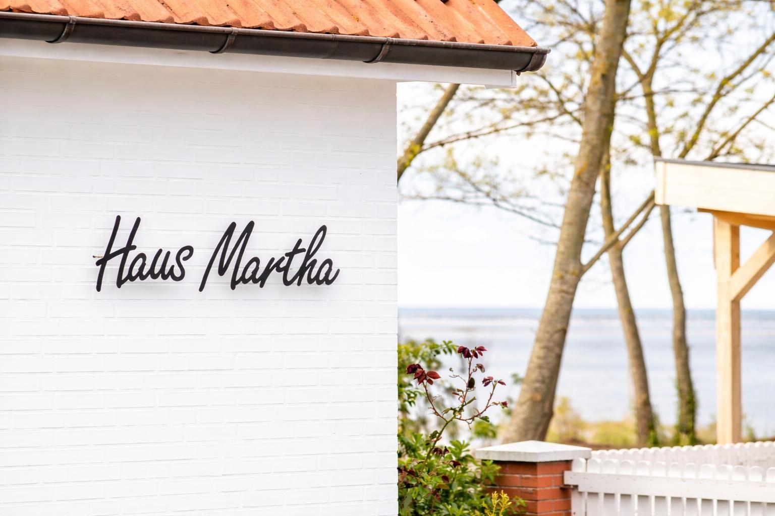 Haus Martha with white wall and red roof, view of water and trees.