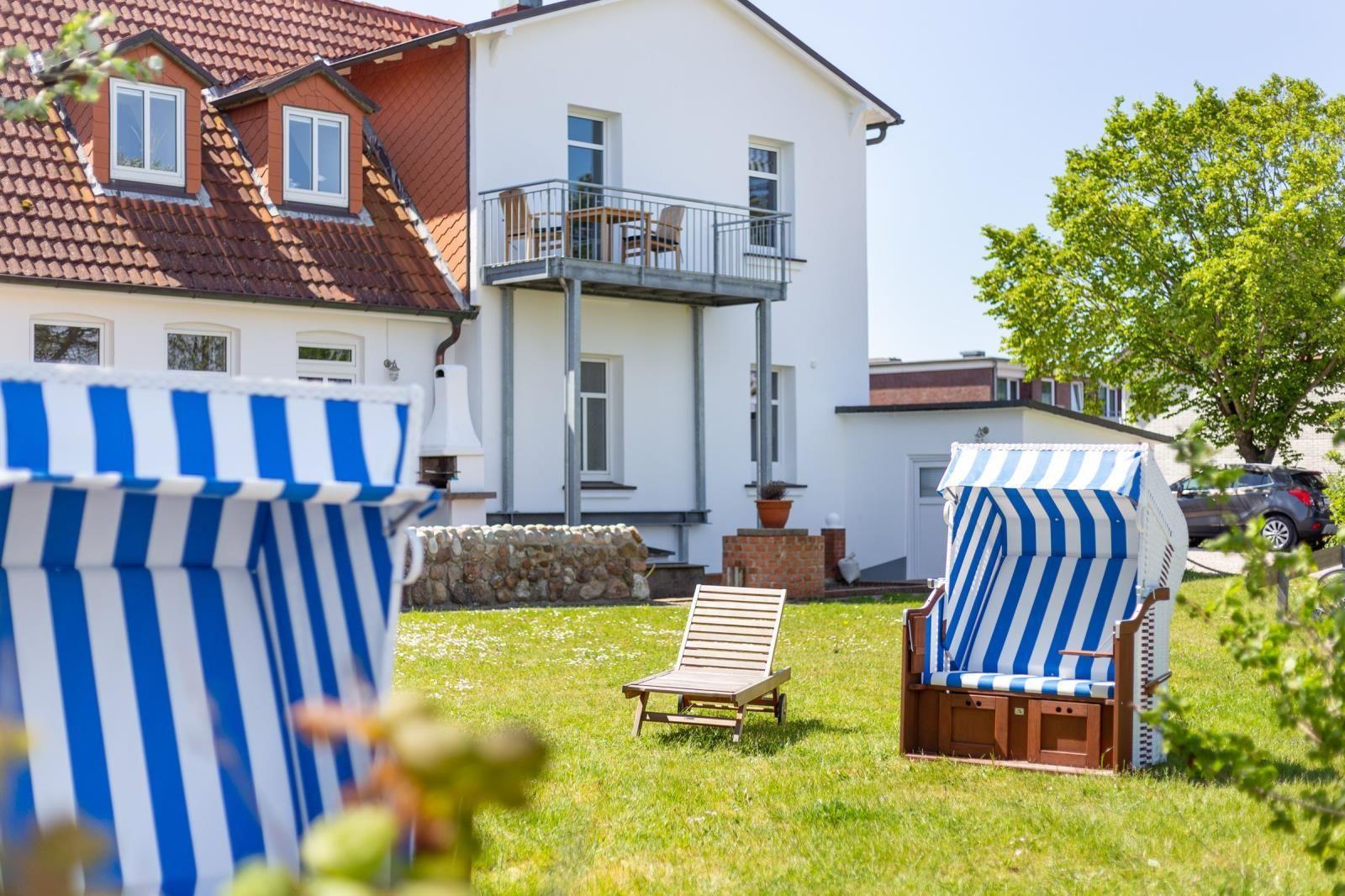 Garden with beach chairs and lounge chair in front of white house with balcony.