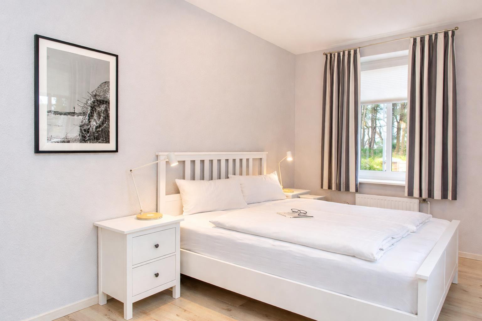 A bedroom with a white bed, nightstands, and a window with curtains.