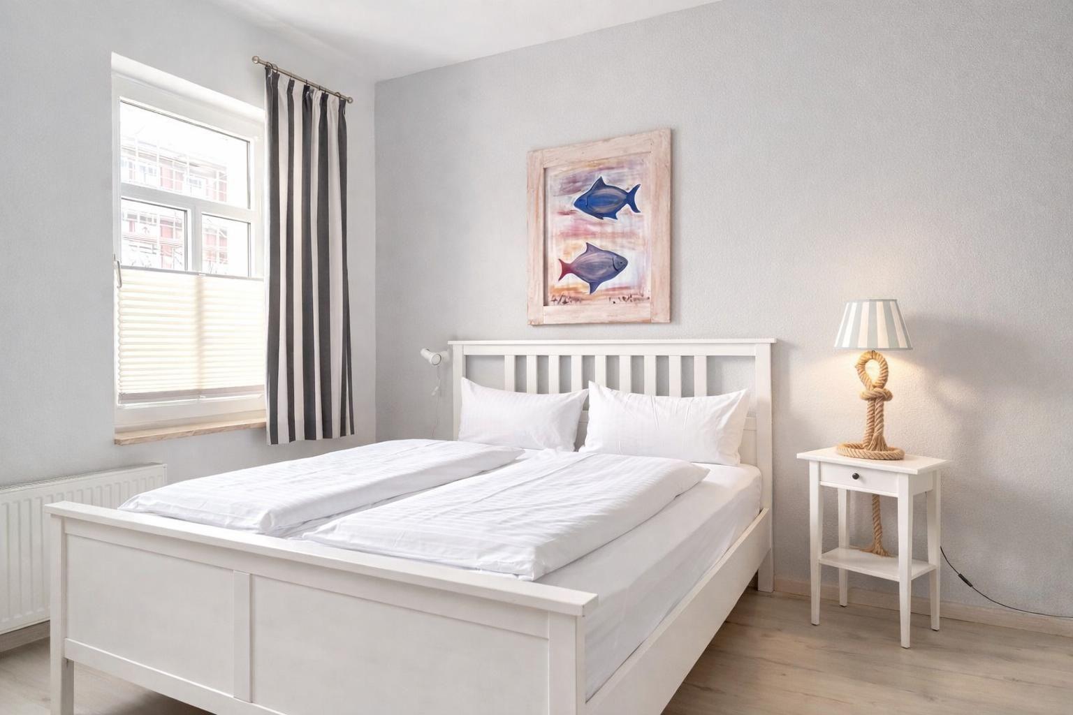 A bedroom with a white bed, fish artwork on the wall, and a nightstand with a lamp.