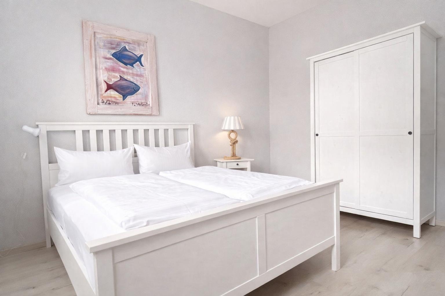 Bedroom with white bed, wardrobe, and wall art with fish.