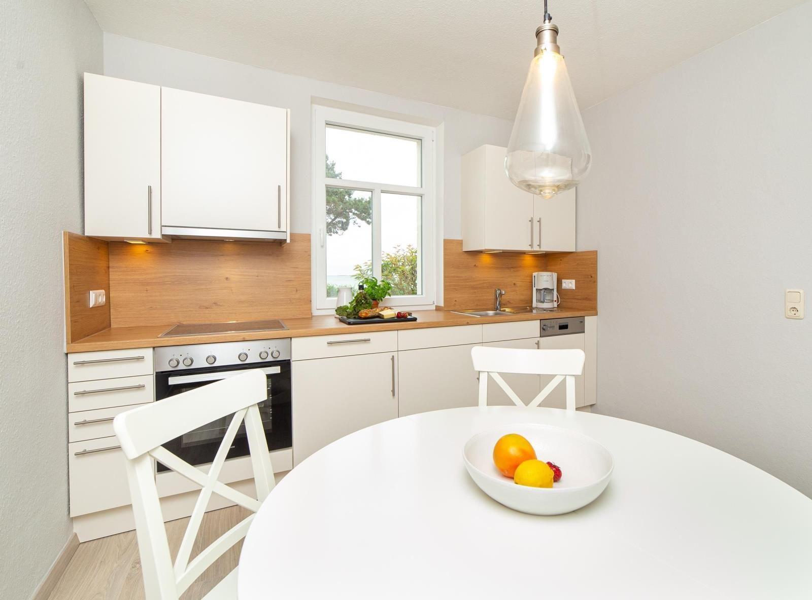 Kitchen with dining area, white cabinets, wooden backsplash, and window view.