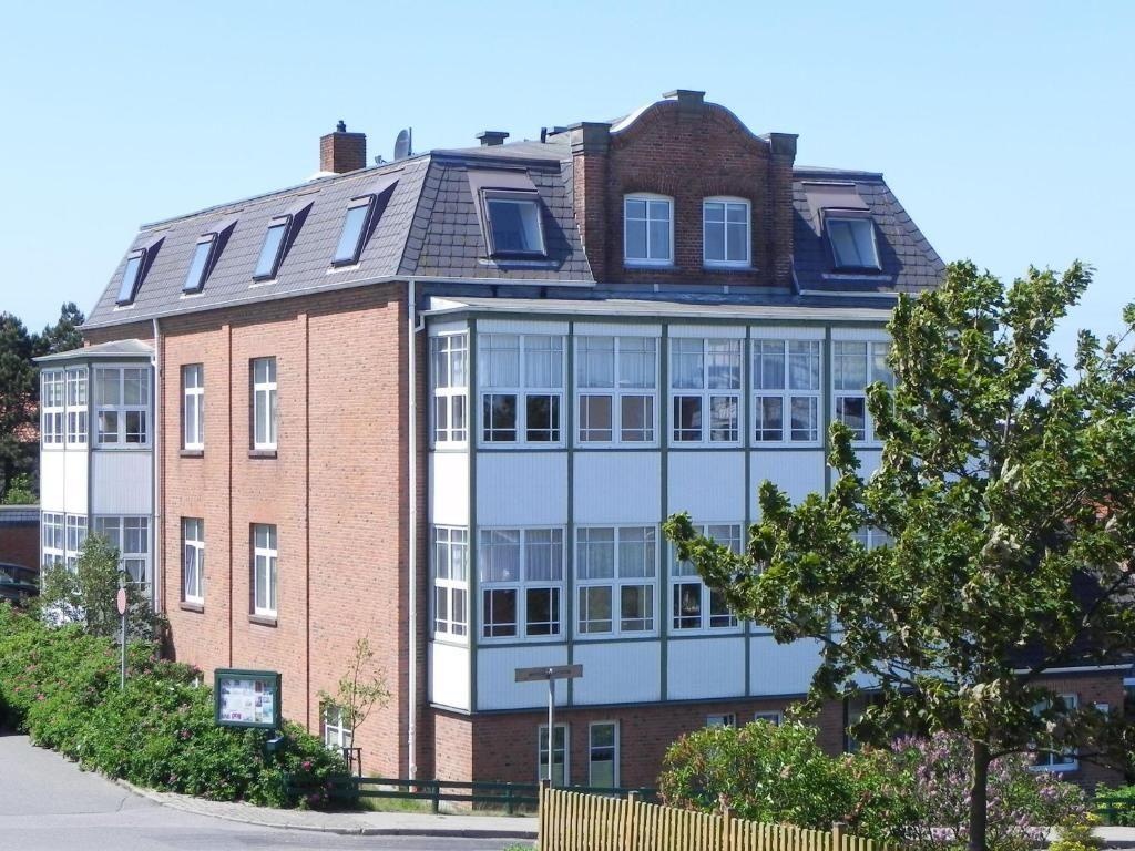 Zweistöckiges Gebäude mit rotem Backstein und weißen Fenstern, Dach mit Dachfenstern, umgeben von Bäumen.