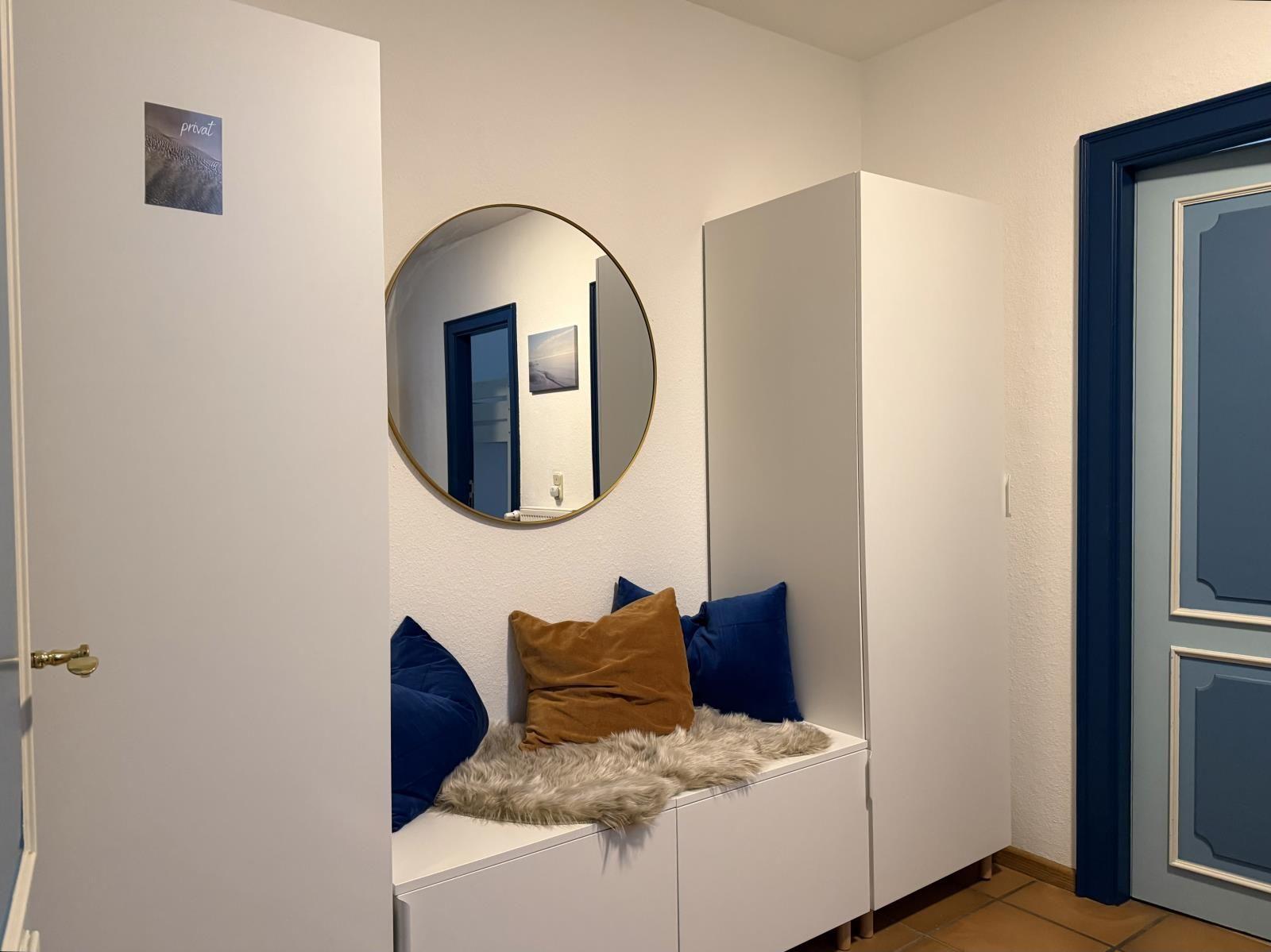 Eingangsbereich mit Sitzbank, Kissen und Spiegel an der Wand.