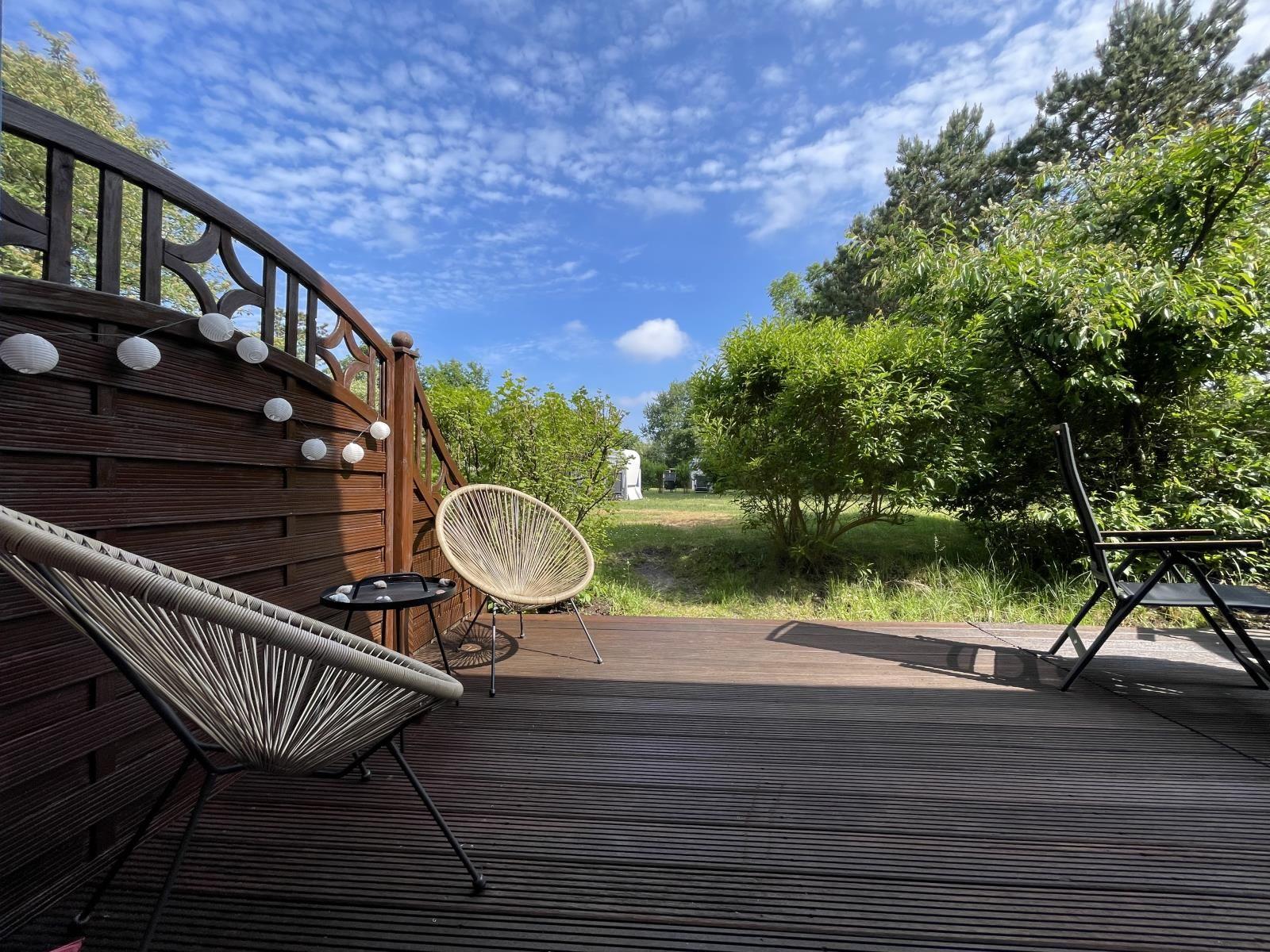 Terrasse mit Sitzgelegenheiten und Blick auf grünen Garten unter blauem Himmel.