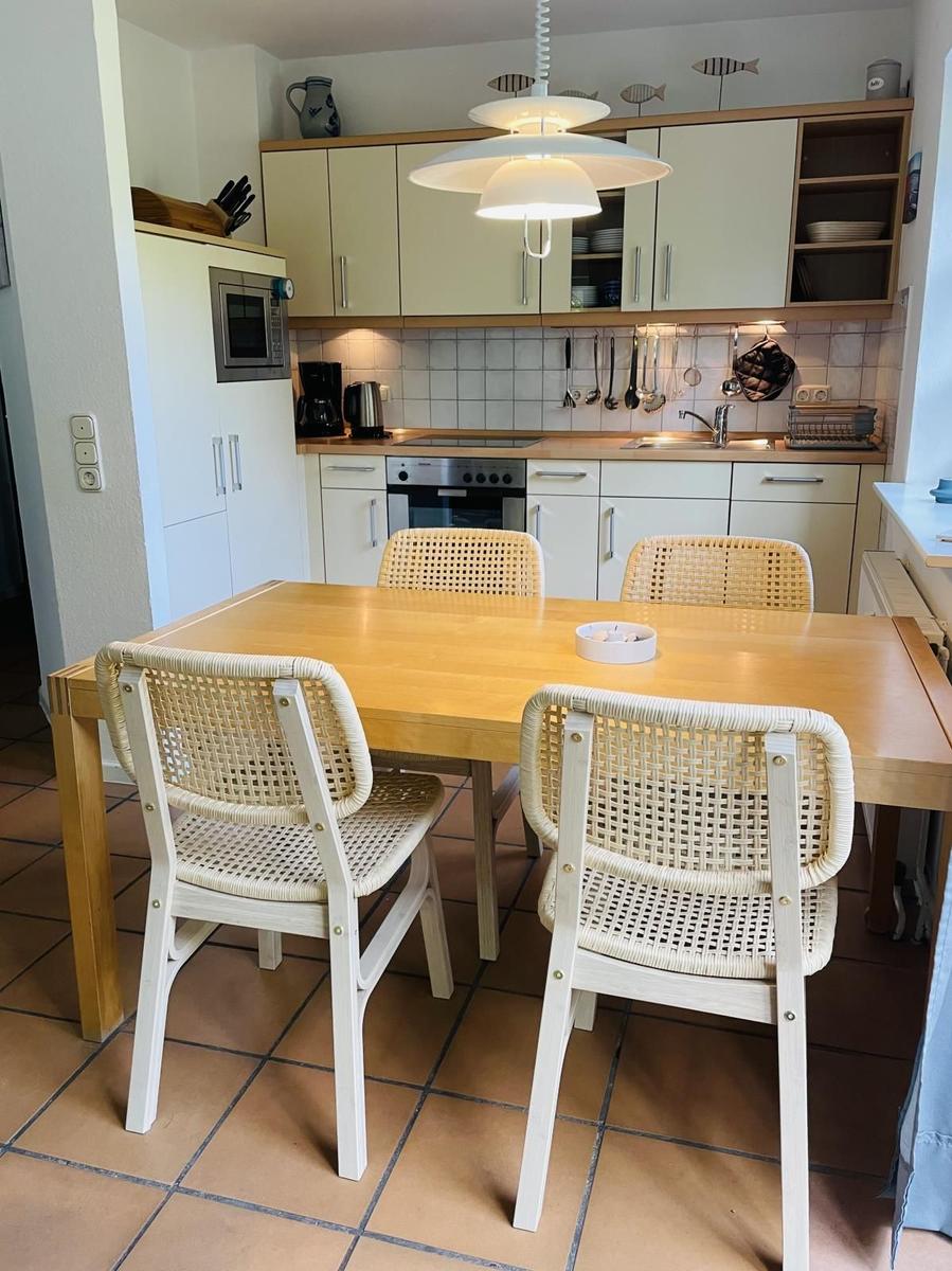 Essbereich mit Holztisch und vier Stühlen. Küche mit weißen Schränken und Kochfeld.