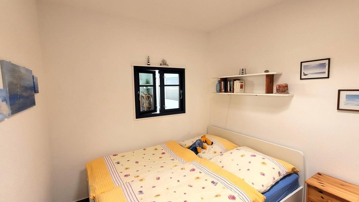 Schlafzimmer mit Bett, Fenster und Regal an der Wand.