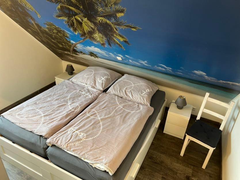 Schlafzimmer mit Doppelbett, Wandbild Strand und zwei Nachttische mit Lampen.