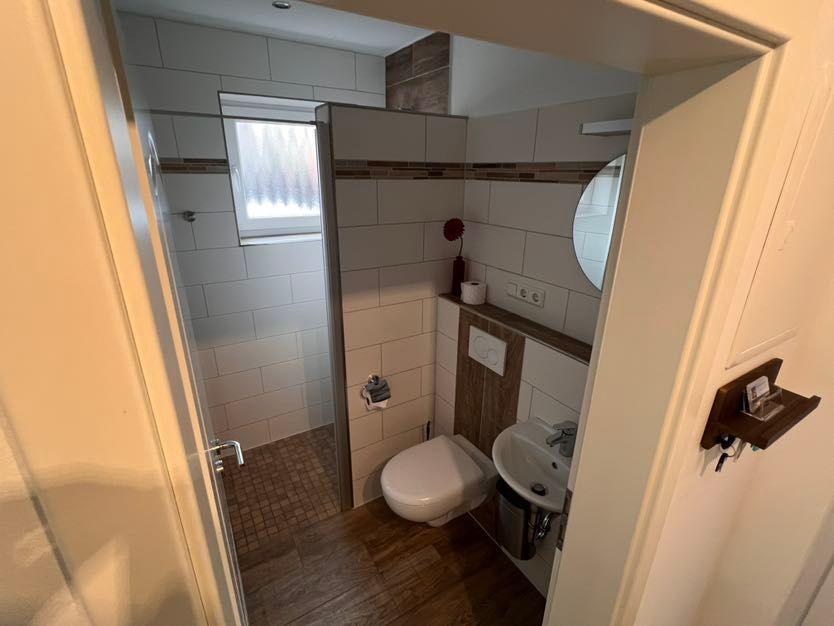 Badezimmer mit Dusche, Toilette und Waschbecken. Fliesenwand und Holzboden.