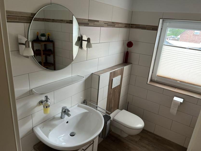 Badezimmer mit Waschbecken, Spiegel und Toilette. Fenster mit Jalousie.