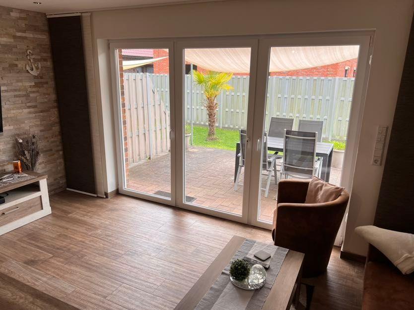Wohnzimmer mit Glasfront zum Garten, brauner Sessel und Holzboden.