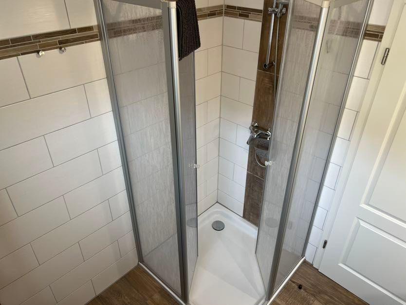 Dusche mit Glaswand, weißen Fliesen und Holzboden