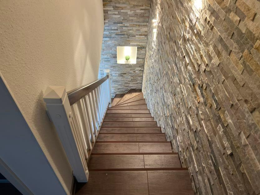 Holzgetäfelte Treppe mit Steinwand und weißem Geländer führt nach oben.