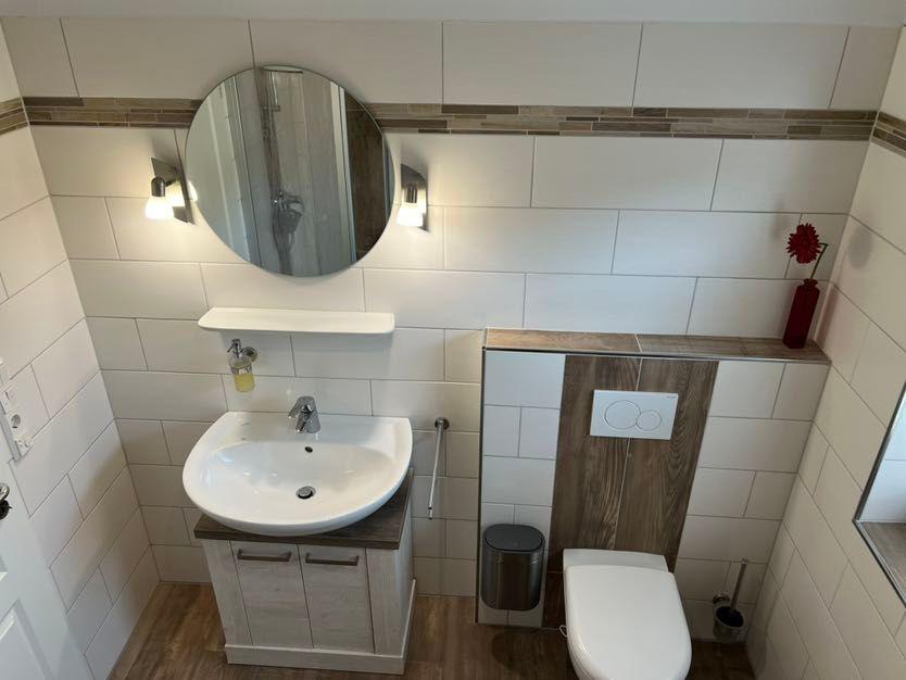 Badezimmer mit Waschbecken, Spiegel und Toilette. Holz- und Fliesenoptik.