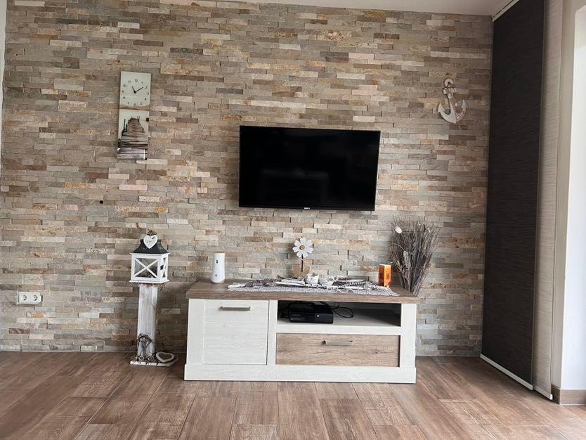 TV-Wand mit Steinverkleidung, weißer TV-Boden und Dekorationsgegenstände.