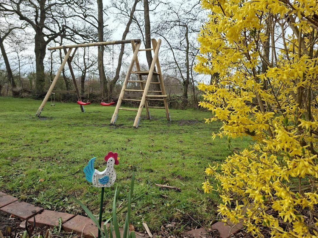 Hinterhof mit Holzschaukel, Blumensträuchern und Hühnerfigur.