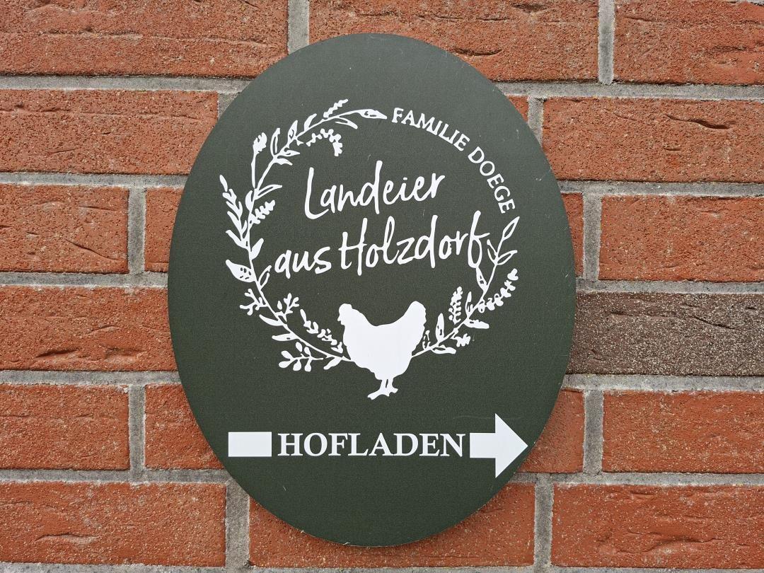 Schild mit Hühnchen und Pflanzenmotiv zeigt Hofladen Richtung rechts.